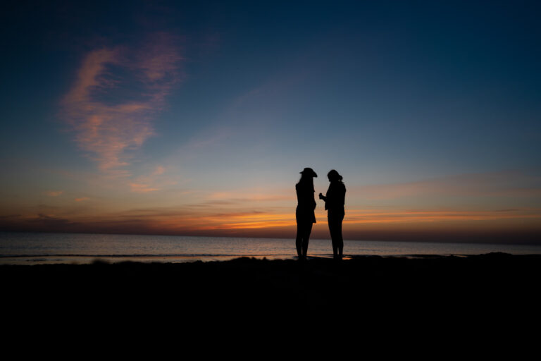 Silhouette von zwei jungen Frauen mit Sonnenuntergang am Meer