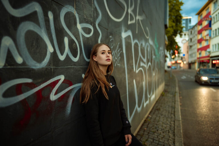 junge Frau steht vor Grafitiwand in der blauen Stunde